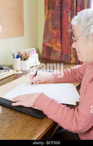 Frau in Ihren Siebzigern Sitzt bin Schreibtisch Und Schreibt Einen Brief Stockfoto