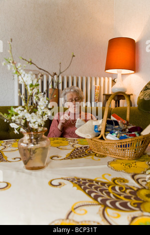 Frau in Ihren Siebzigern Sitzt Im Wohnzimmer Und Stopft Wollsocken Stockfoto