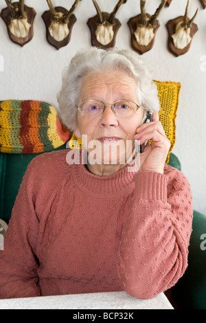 Frau in Ihren Siebzigern Sitzt Auf Einem Sofa Im Wohnzimmer Und Telefoniert Mit Einem Handy Stockfoto