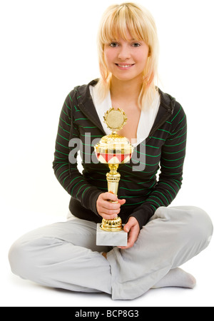 Junge Frau in Sportkleidung Sitzt Im Schneidersitz Und Hält Lachend Einen Pokal Stockfoto