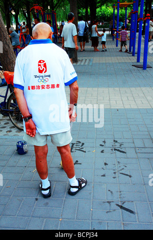 Alte chinesische Mann in 2008 Beijing Olympic Volunteer Uniform üben Kalligraphie auf dem Boden in einem Park, Peking, China Stockfoto