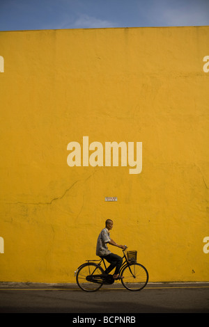 Ein Mann reitet auf seinem Fahrrad durch eine gelbe Wand in Melacca Malaysia Stockfoto