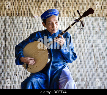 Eine vietnamesische Mann in traditioneller Kleidung, die ein Instrument spielen Stockfoto