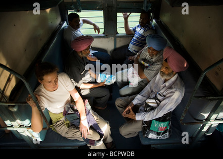 Westeuropäische Pkw sitzen mit lokalen Passagiere in einem Sleeper Abteil, wo die Betten als Sitze festgelegt sind. Indische Zug. Stockfoto