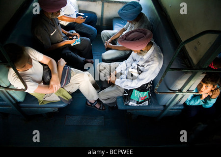 Westeuropäische Pkw sitzen mit lokalen Passagiere in einem Sleeper Abteil, wo die Betten als Sitze festgelegt sind. Indische Zug. Stockfoto