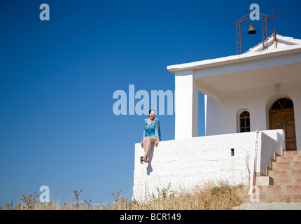 Frau in blau Kaftan sitzt auf weißen Kapelle Wand in Griechenland Stockfoto