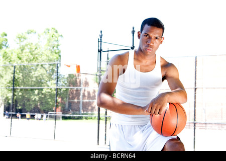 Schön sportlich afroamerikanische männliche Basketballspieler mit Haltung gekleidet in weißen stehend mit seinem Ball im Freien im Sommer Stockfoto