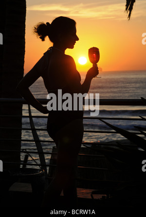 Silhouette einer jungen Frau mit einem Glas trinken stand vor atemberaubenden Sonnenuntergang über dem Horizont über den Indischen Ozean. Stockfoto