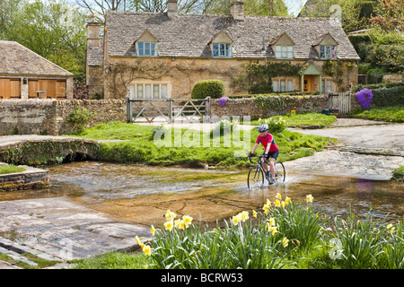 Ein Radfahrer, der durch die furt über das River Eye im Cotswold-Dorf Upper Slaughter, Gloucestershire, Großbritannien, fährt Stockfoto