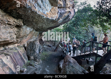 Eine Gruppe von Touristen einen Vortrag anhören und mit Blick auf die Aborigine-Felskunst in der Anbangbang Gallery am Nourlangie Rock. Kakadu NP Stockfoto