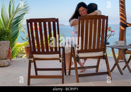 Romantisches Paar Liebkosungen in Teak Liegestuhl und genießen Sie ihren Kaffee am Morgen und einen weitläufigen Blick auf den Pazifischen Ozean. Stockfoto