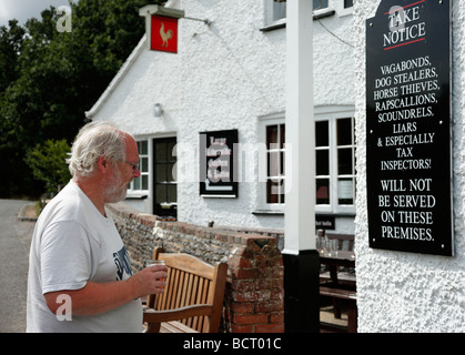 Mann liest eine amüsante Mitteilung außerhalb der Gerste Mähen Gastwirtschaft, Tilford, Surrey, England, UK. Stockfoto