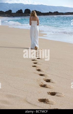 Eine Frau geht entlang des Strandes hinterlassen Spuren im sand Stockfoto