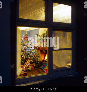 WEIHNACHTSGESCHENKE UNTER DEM BAUM UND KAMIN GESEHEN DURCH FENSTER IN DER NACHT Stockfoto