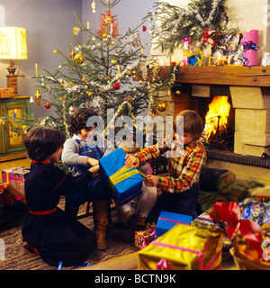 3 KINDER ERÖFFNUNG WEIHNACHTEN UNTER DEM BAUM Familie Weihnachtsgeschenke Baum öffnen PRÄSENTIERT Stockfoto