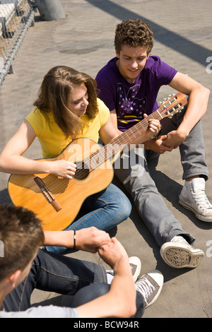 Mädchen spielt die Gitarre, zwei jungen hören Stockfoto