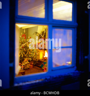 WEIHNACHTSGESCHENKE UNTER DEM BAUM UND KAMIN GESEHEN DURCH FENSTER IN DER NACHT Stockfoto