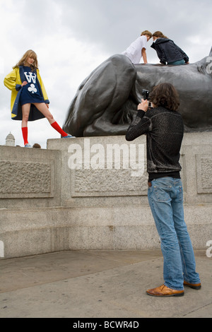 Ein junger Mann fotografiert eine hübsche blonde Mädchen in einem gelben Mantel und rote Kniestrümpfe Socken von den Löwen auf dem Trafalgar Square posiert Stockfoto