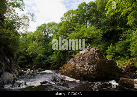 Junges Paar sitzt auf Rock Fairy Glen-Schlucht Conwy River im Juli Sonnenschein im Sommer in der Nähe von Betws-y-Coed North Wales Cymru UK Stockfoto