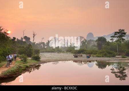 Radfahrer und ein Traktor in der Morgendämmerung; Rush Hour auf dem Lande in der Nähe von Vang Vieng, Laos Stockfoto