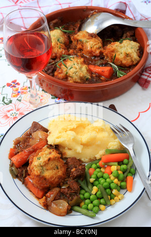 Ein Gericht mit Rindfleisch-Eintopf mit Petersilie Knödel Kartoffelpüree und Mischgemüse mit Roséwein und die Schüssel hinter Stockfoto