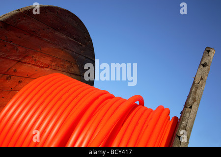 Orangefarbene Kabel für Breitbandverbindungen auf einer hölzernen Kabeltrommel vor blauem Himmel. Stockfoto