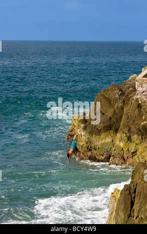 Junger Mann taucht aus Betonplattform in Wasser als Touristen Uhr entlang des Malecon, Mazatlan, Mexiko Stockfoto