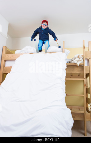 Junge mit Ski auf Bett Stockfoto