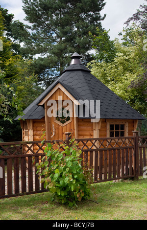 Sechseckig gefliester Gartenschuppen aus Holz mit Kamin, Filzgefliestem Dach und Grenzzaun; Deeside Log Cabins, Aberdeenshire, Schottland, Großbritannien Stockfoto