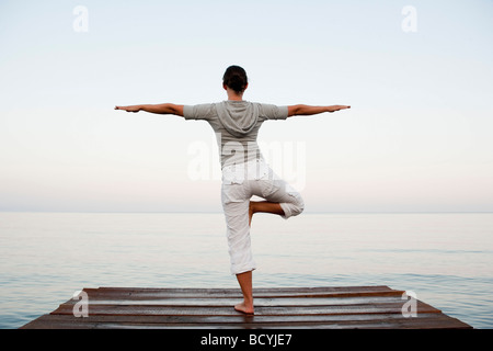 Junge Frau beim Yoga am Steg Stockfoto