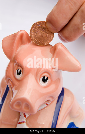 Ein Mann legt einen Cent in ein Sparschwein. Dies ist Maxwell, eines aus einer Reihe von fünf Sparschweine in den 1980er Jahren von der NatWest Bank produziert. Stockfoto