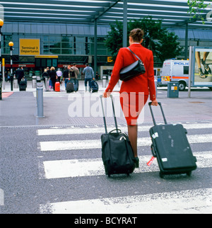 Hintere Ansicht Rückseite eines Air Hostess Frau mit Gepäck auf einem Zebrastreifen zu Fuß zum Terminal 3 Eingang am Heathrow Airport London England KATHY DEWITT Stockfoto