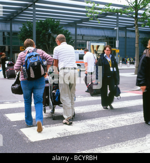 Rückansicht ältere Passagiere, die ihr Gepäck auf dem Wagen zum Eingang des Abflugterminals vor dem Flughafen Heathrow London bringen Stockfoto