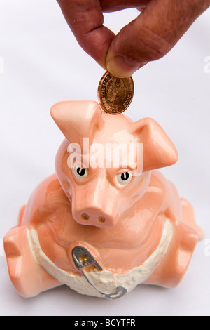 Ein Mann legt einen Cent in ein Sparschwein. Dies ist Woody, eines aus einer Reihe von fünf Sparschweine in den 1980er Jahren von der NatWest Bank produziert. Stockfoto