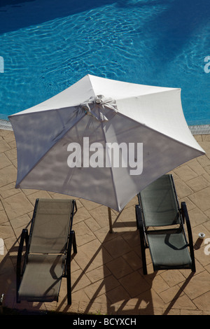 Zwei Sonnenliegen mit Sonnenschirm neben einem großen Schwimmbad Stockfoto