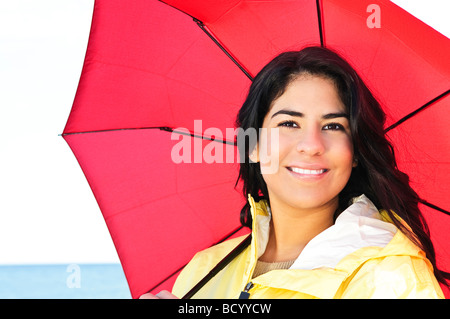 Porträt von schönen lächelnden Brünette Mädchen tragen gelben Regenmantel mit roten Regenschirm Stockfoto