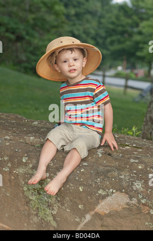 zwei Jahre alten Jungen spielen in einem Park mit einem Spielzeug-LKW auf einem Felsen sitzen. Er hat einen Safari-Hut auf. Stockfoto