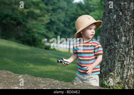 zwei Jahre alten Jungen spielen in einem Park mit einem Spielzeug LKW stehen durch einen Baum. Er hat einen Safari-Hut auf. Stockfoto