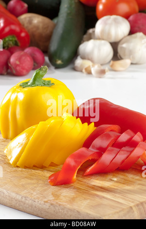 Schneiden Sie Paprika in Scheiben, auf Holzbrett mit einem Haufen von Gemüse im Hintergrund Stockfoto