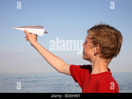 Teenager bereit, einen Papier-Dartpfeil bei Sonnenuntergang über dem Meer zu werfen. Stockfoto