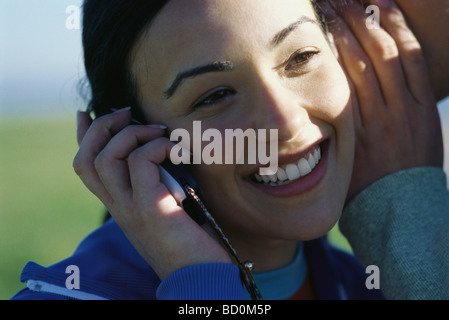 Junge Frau mit Handy, Mann flüstert in ihr Ohr Stockfoto