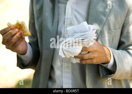 Person, die die Hälfte gegessen, Gebäck in einer Hand und Einweg-Becher und Papierservietten in der anderen hand Stockfoto