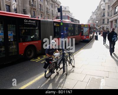 Radfahrer, die Auspacken sein Fahrrad in London s Regent Street mit Bussen im Hintergrund London UK Stockfoto