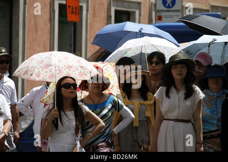 orientalische Touristengruppe mit Sonnenschirmen in der heißen Sonne in Rom Italien Stockfoto