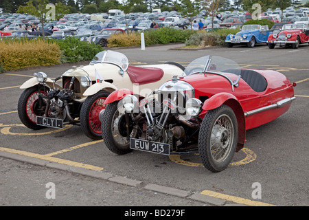 Zwei Morgan 3 Wheeler Motorwagen rot- und parkte vor zwei moderne Morgan-Sportwagen bei Jubiläumsfeier Che Stockfoto