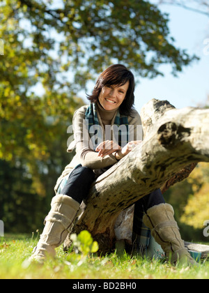 Frau sitzt auf Log im Herbst Stockfoto