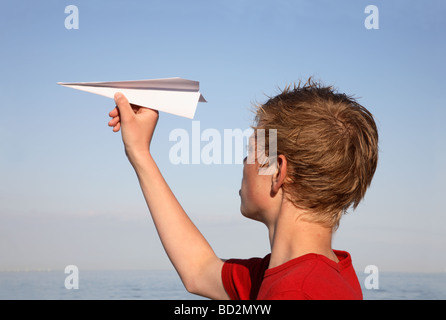 Teenager bereit, einen Papier-Dartpfeil bei Sonnenuntergang über dem Meer zu werfen. Stockfoto