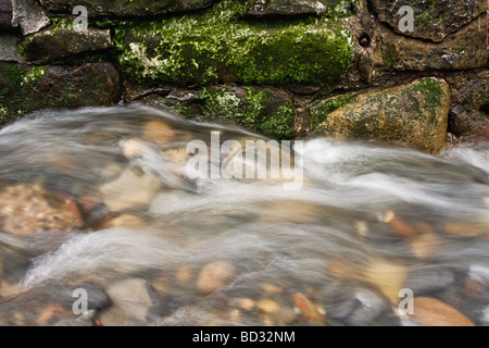 Foto von schnell bewegten Wasser fließt gegen eine Wand über Felsen und Kieselsteine. Stockfoto