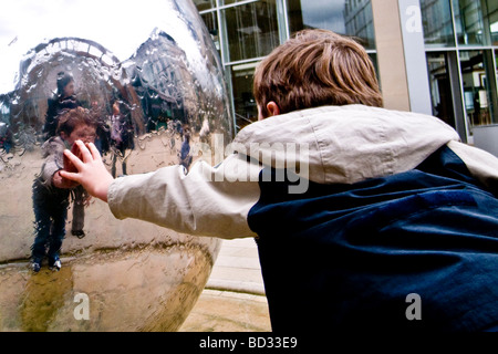 Ein Junge berührt eines der Orb-Ornamente in Peace Gardens, Sheffield, direkt vor dem Wintergarten. Stockfoto