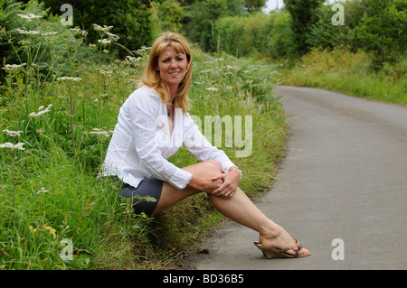 Reife Frau trägt ein weißes Hemd und Rock sitzt am Straßenrand Stockfoto